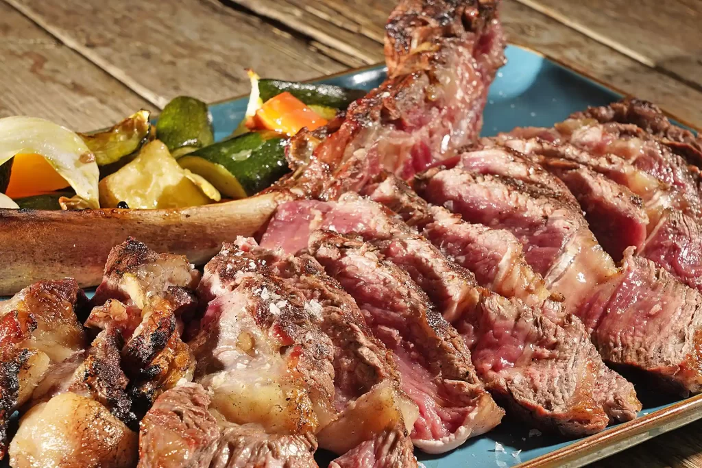 Sliced grilled meat with roasted vegetables on a plate.