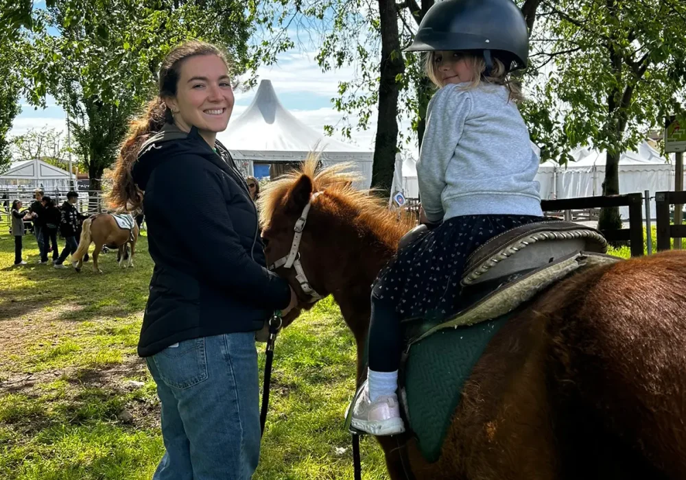 Una donna guida un pony su cui è seduta una bambina in un'area all'aperto.