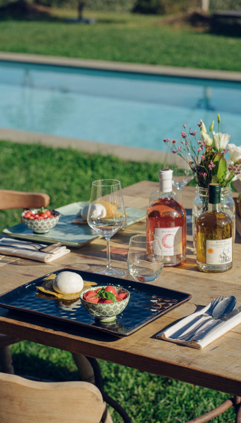 Tavolo all'aperto apparecchiato con cibo e vino vicino a una piscina.