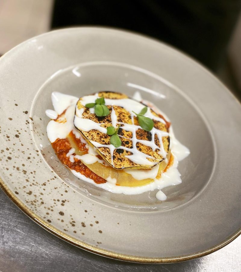 Un elegante piatto di melanzane grigliate con salsa cremosa e guarnizioni di erbe fresche.