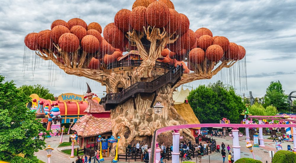 Un grande albero stilizzato con passerelle e sfere arancioni in un parco di divertimenti.